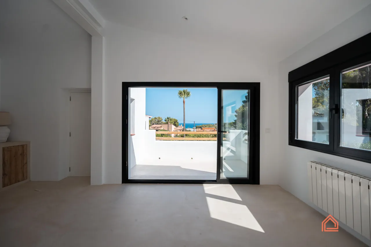 After: Renovated room with microcement floor and glass doors opening to a sea-view terrace