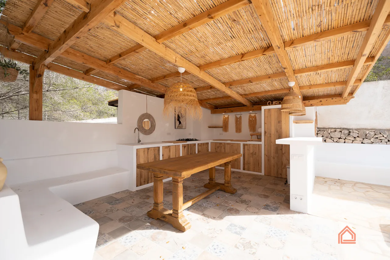 Outdoor kitchen under a reed and timber pergola with rustic dining table and patterned tiles