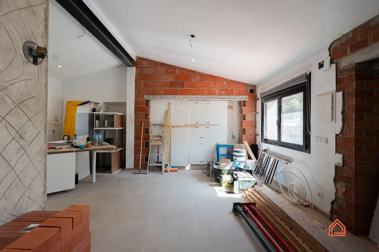 Before: Open-plan room before renovation, with exposed brick, rough walls and stored materials